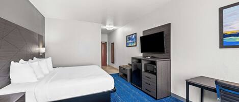 A hotel room with a bed, a desk, a TV, and a painting on the wall.