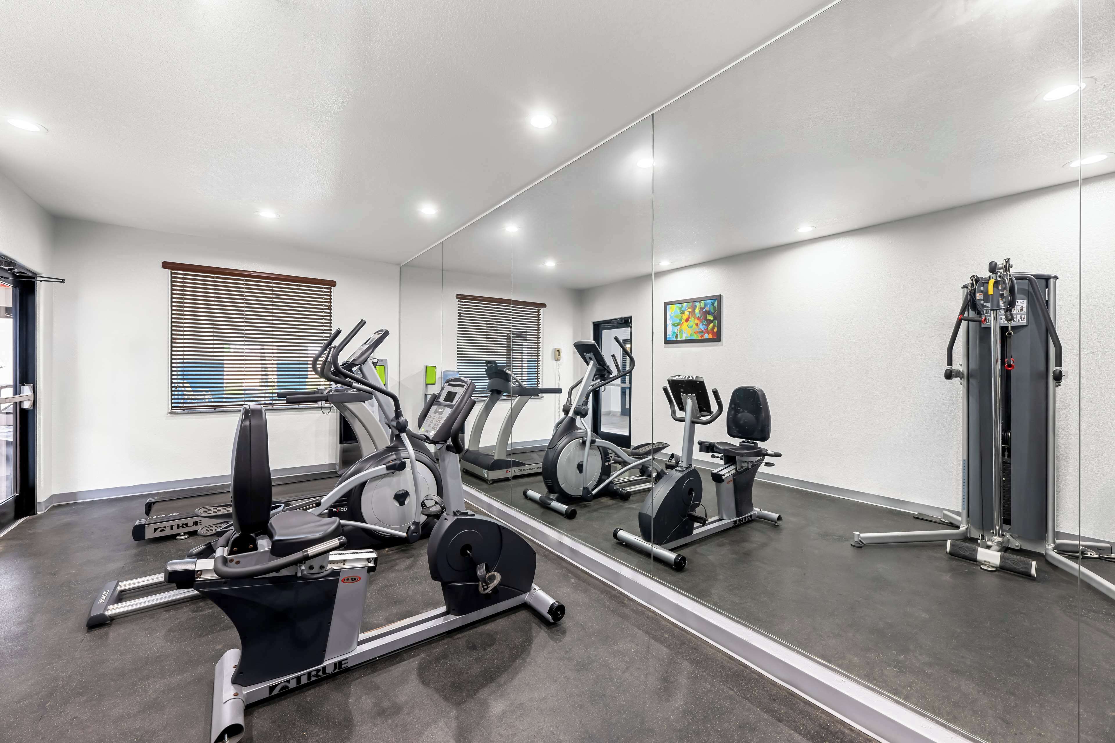 A gym with cardio machines, weight equipment, and a large mirror.