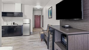 A modern kitchen with dark cabinetry, a built-in microwave, and a large flat-screen TV mounted on the wall.