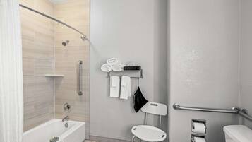 A modern bathroom with a bathtub, shower, toilet, and a handrail.