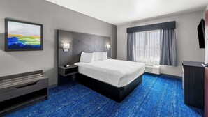 A hotel room with a large bed, a desk, a chair, and a window with curtains.