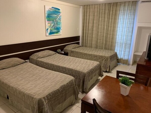 Une chambre d’hôtel avec deux lits simples, une table en bois avec des chaises, une petite plante en pot et un tableau au mur.