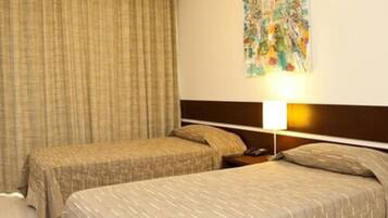 A hotel room with two single beds, a headboard, a bedside table with a lamp, and a curtain.