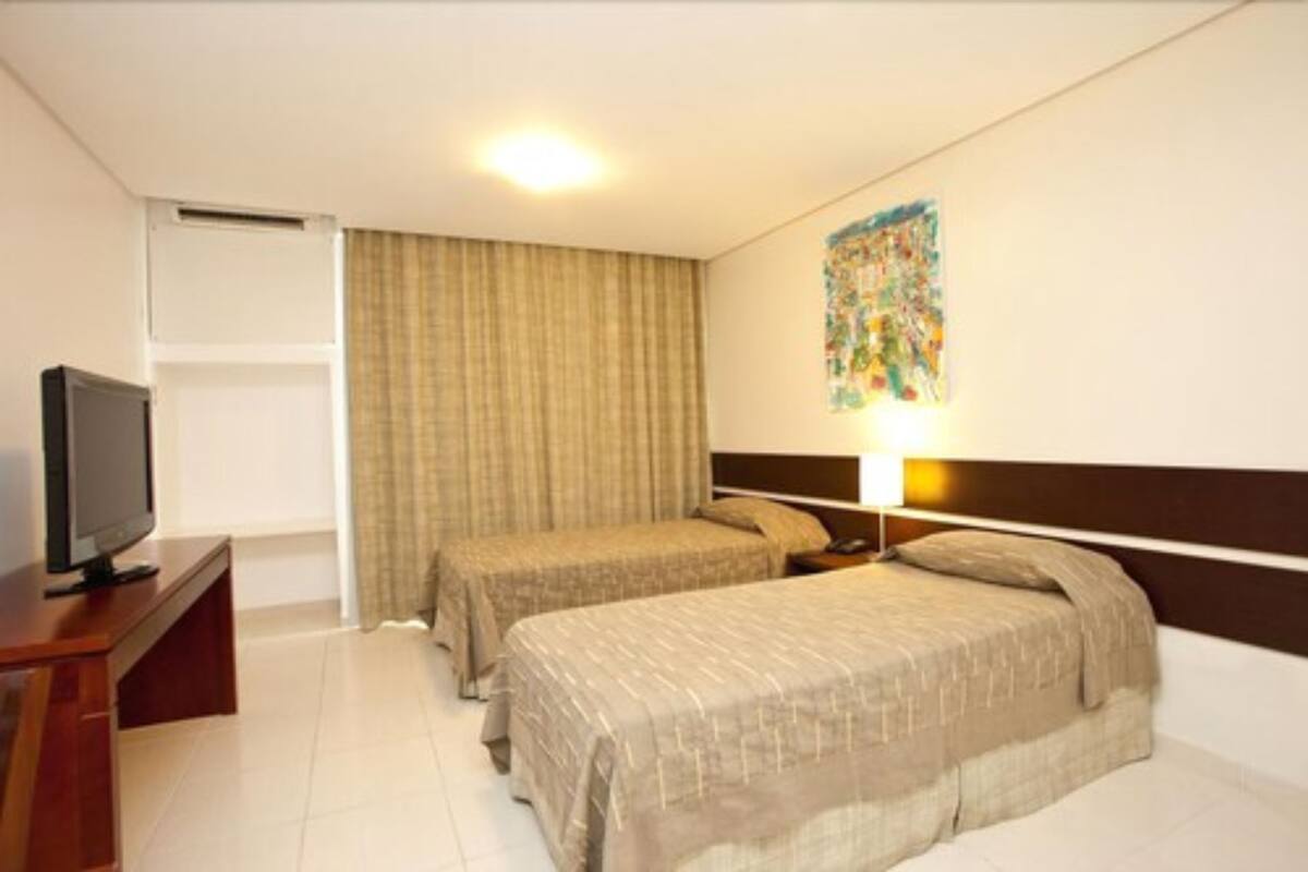 Camera d'albergo con due letti, una televisione, un quadro appeso al muro e una finestra con tende.