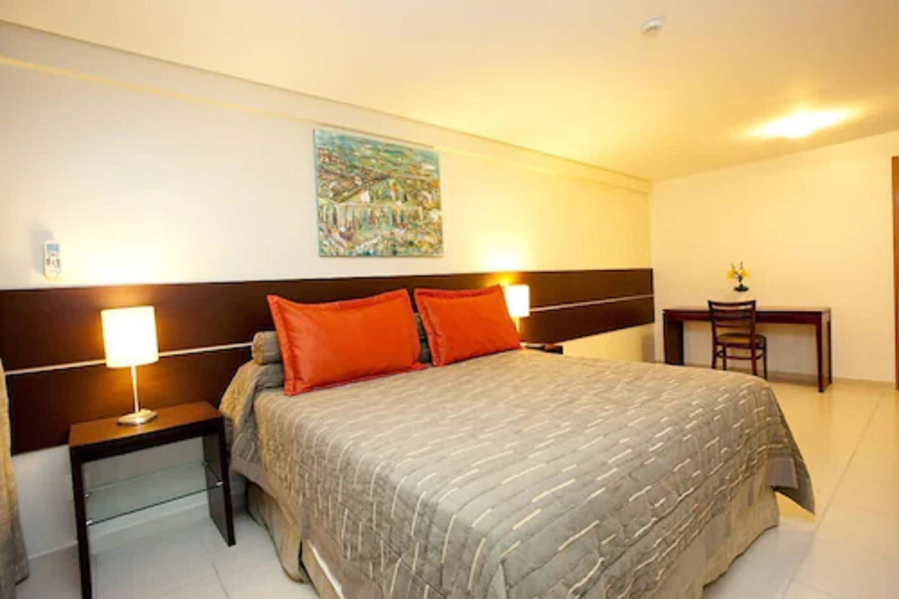 A neatly arranged hotel room with a large bed, two bedside tables with lamps, a desk, and a chair.