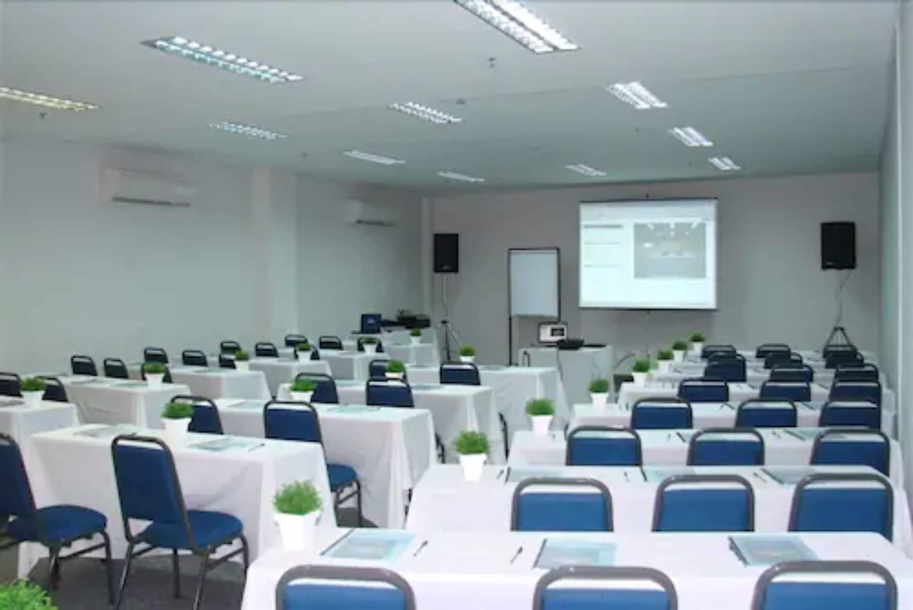 A conference room with rows of tables, chairs, and a projector screen.