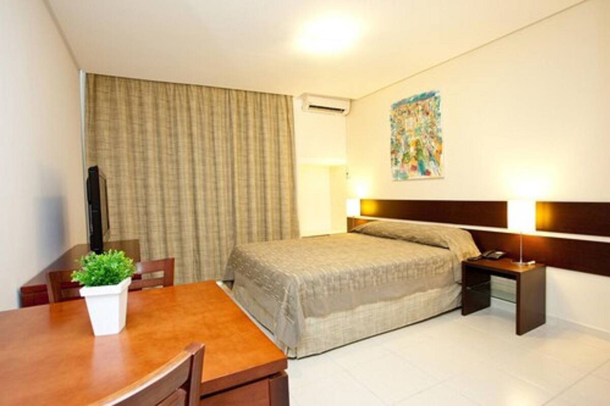 Camera d'albergo con un letto, una scrivania, una sedia, una pianta in vaso, una lampada e un quadro appeso al muro.
