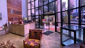 A lobby with a reception desk, a patterned armchair, and large windows offering a view of the street. - América Towers Hotel (Salvador)