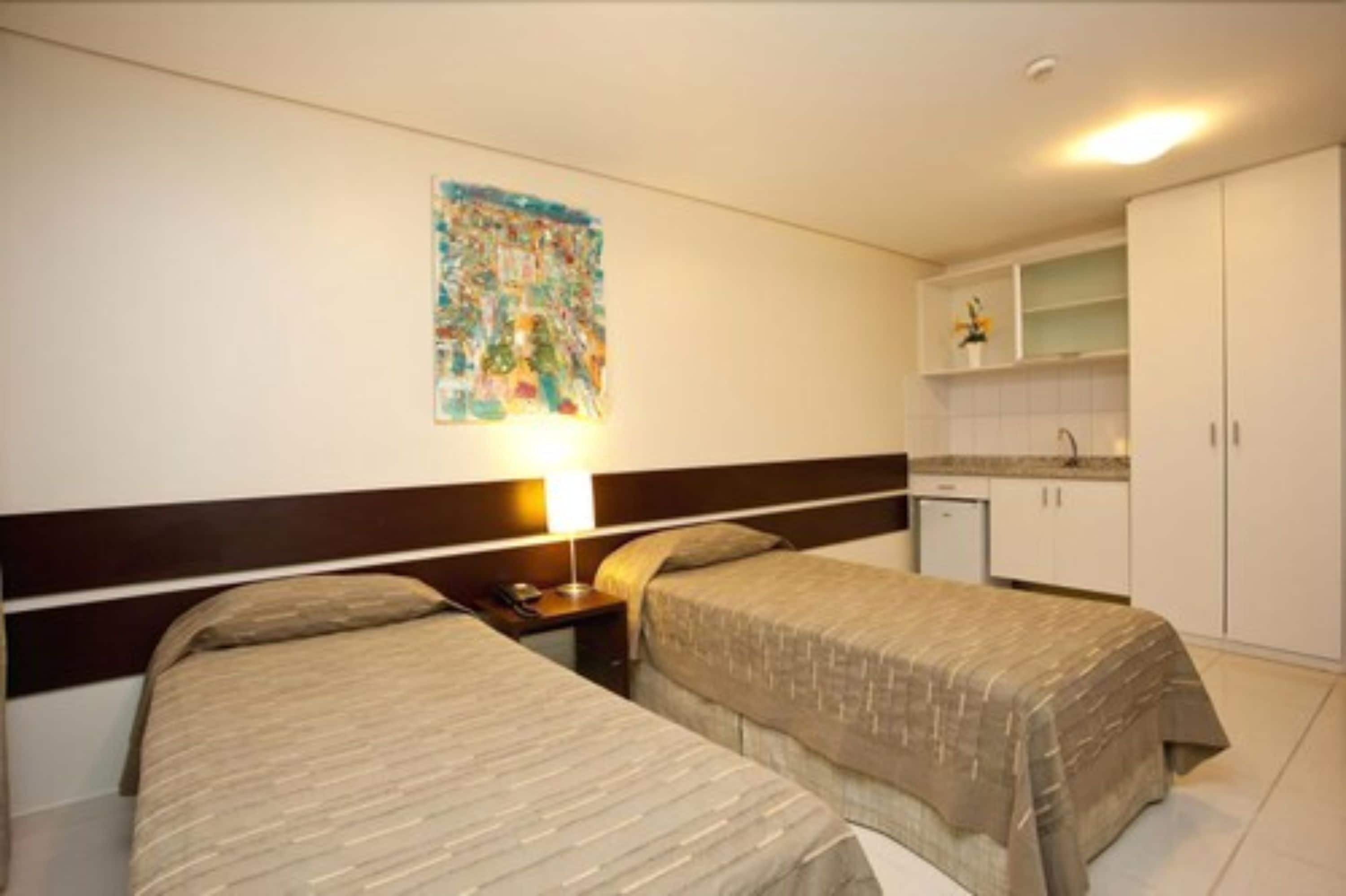 A hotel room with two beds, a small kitchenette, and a wall-mounted artwork.