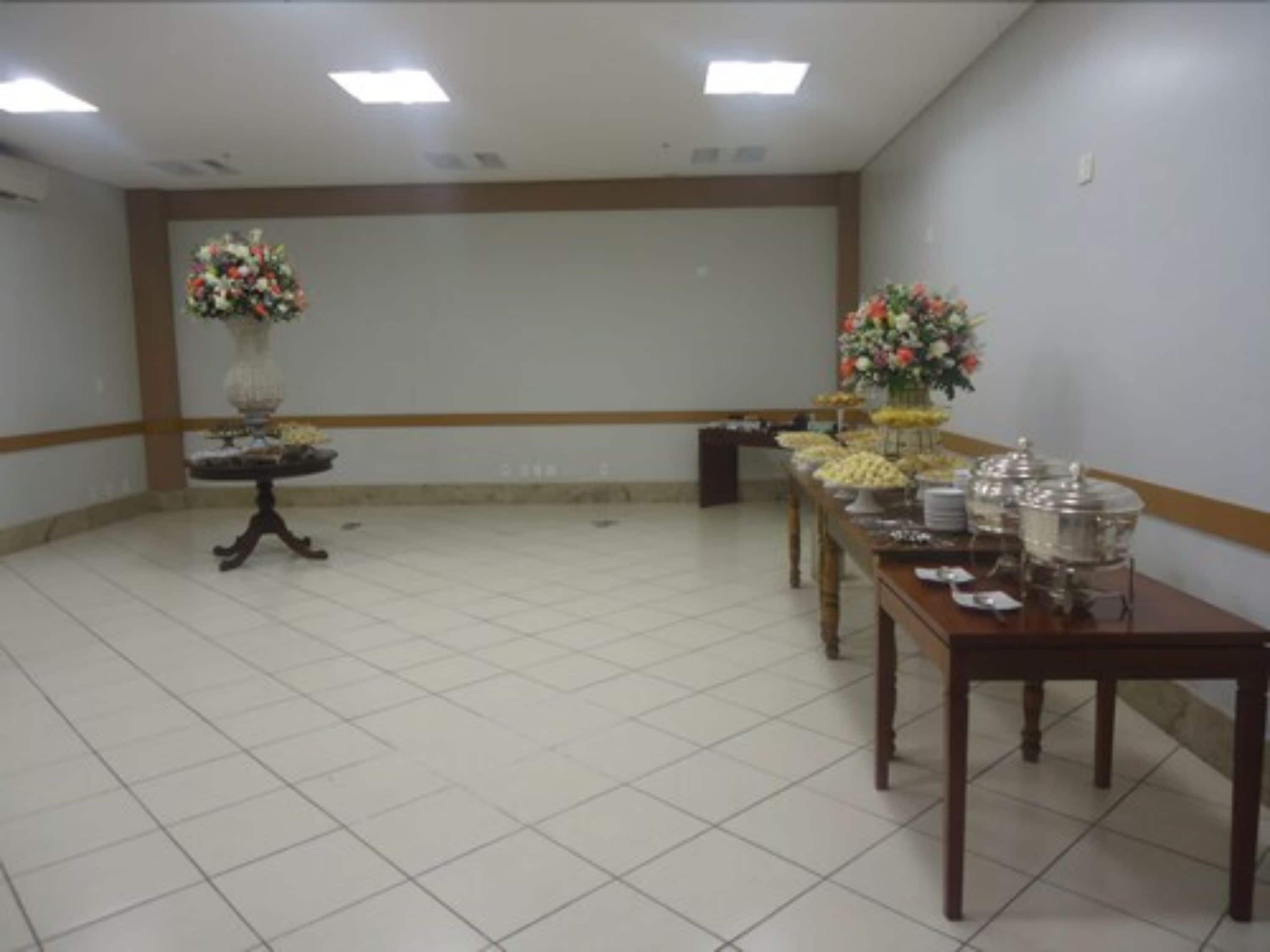 Un salón de conferencias con una larga mesa dispuesta para un bufé, dos centros de mesa florales y un piso de baldosas.