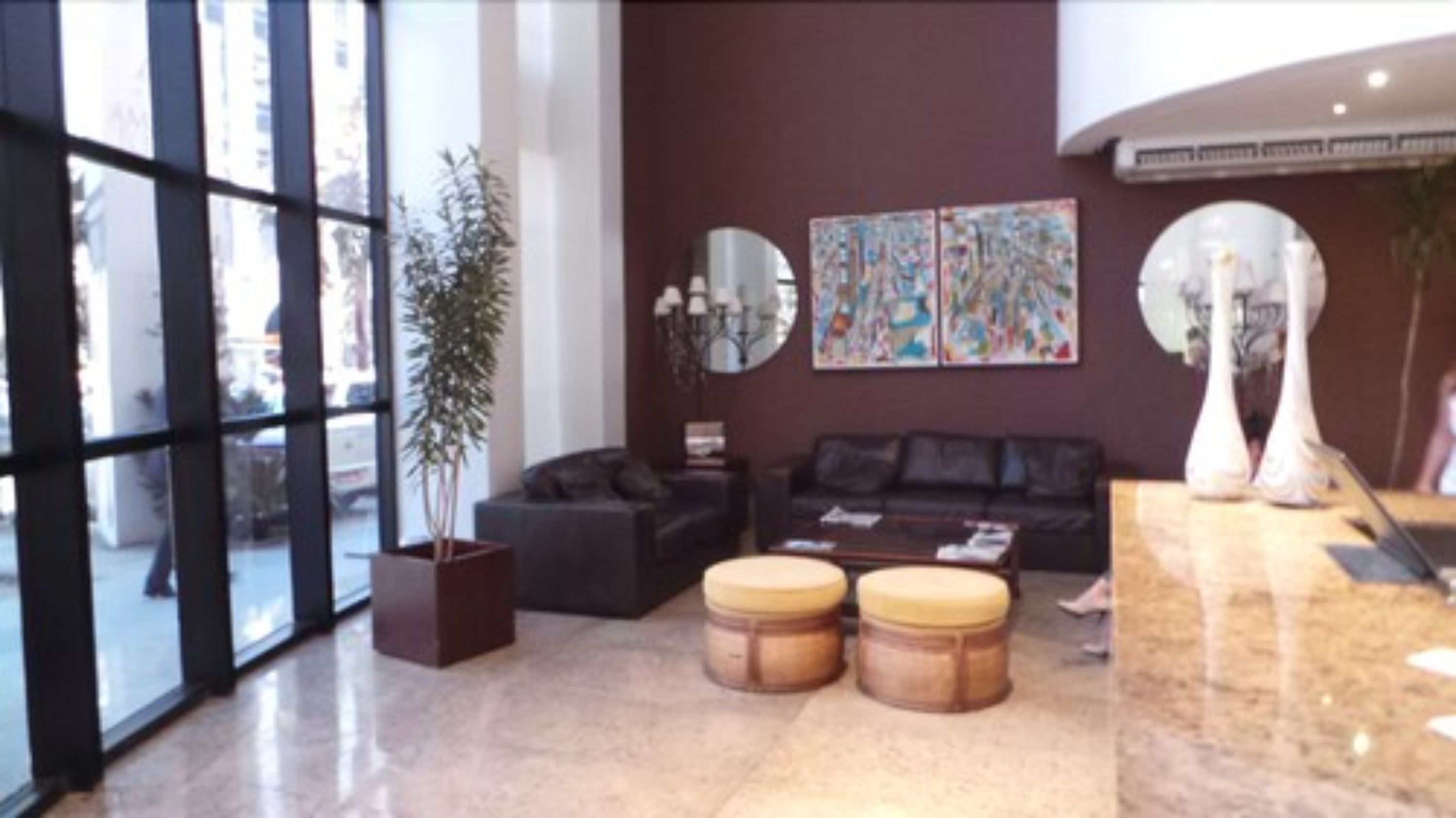 Un'accogliente hall moderna con una grande finestra, una comoda poltrona nera, due poggiapiedi in legno, una pianta in vaso e un'opera d'arte astratta appesa al muro.