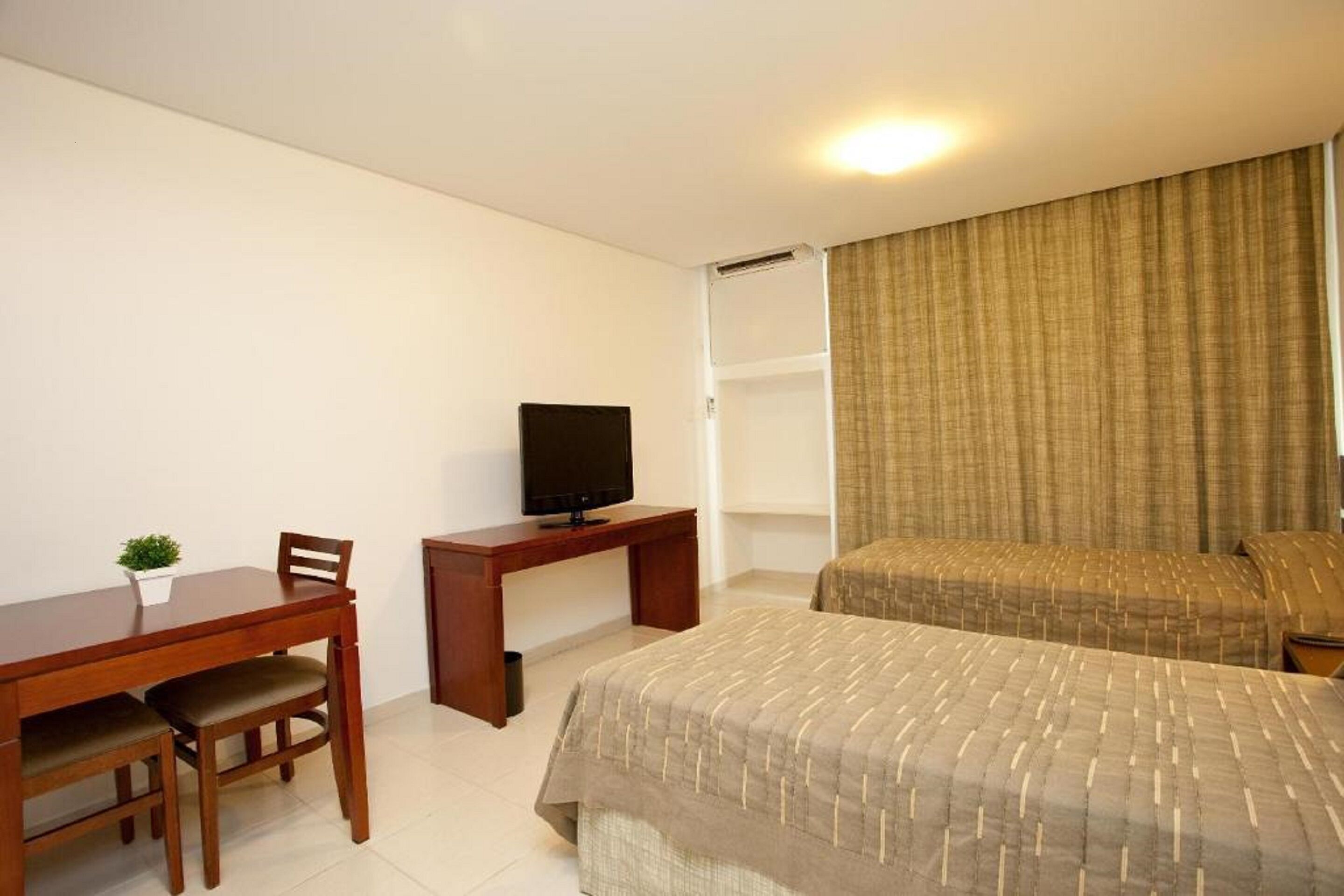 Een hotelkamer met een houten bureau, een televisie, een bed met een gestreept sprei en een kleine plant op het bureau.