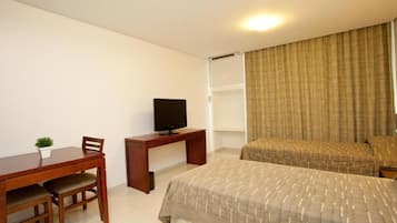 Een hotelkamer met een houten bureau, een televisie, een bed met een gestreept sprei en een kleine plant op het bureau.