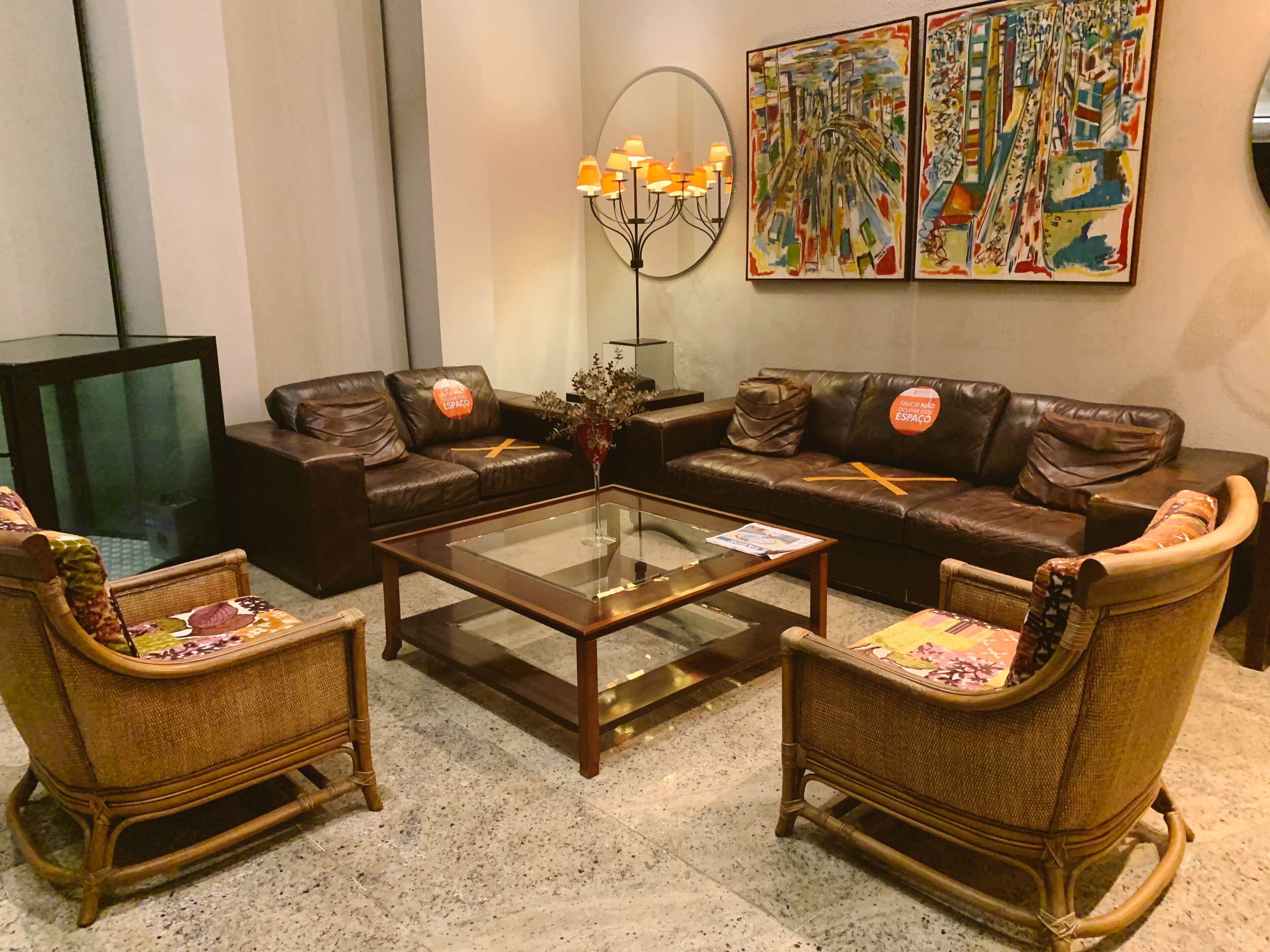 Ein Wohnzimmer mit einem Glastisch, zwei Korbsesseln, einem braunen Ledersofa, einem Fernseher und zwei Bildern an der Wand.