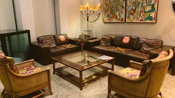 Ein Wohnzimmer mit einem Glastisch, zwei Korbsesseln, einem braunen Ledersofa, einem Fernseher und zwei Bildern an der Wand.