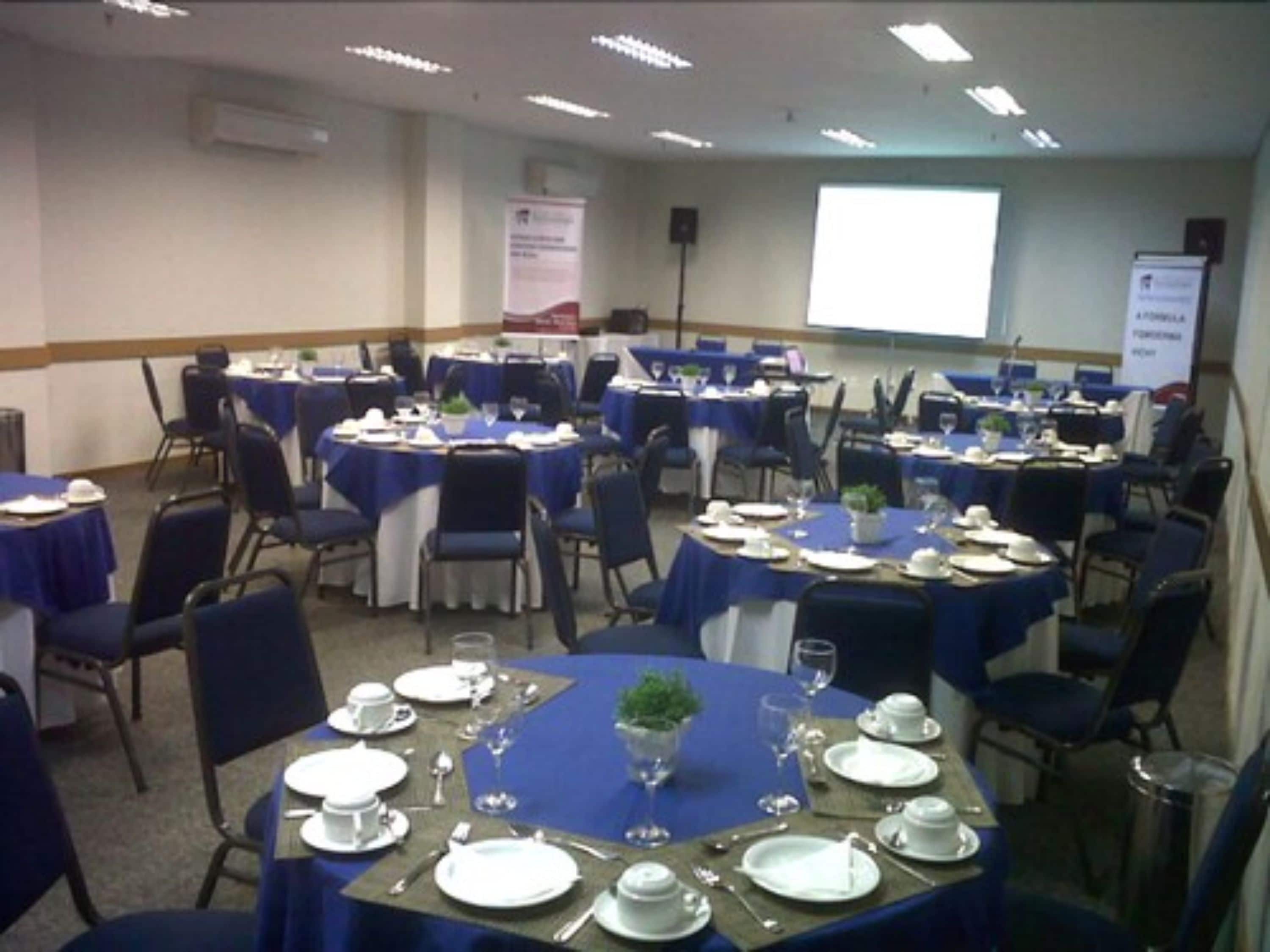 A conference room with multiple tables set for a meeting, equipped with chairs, tables, and presentation screens.