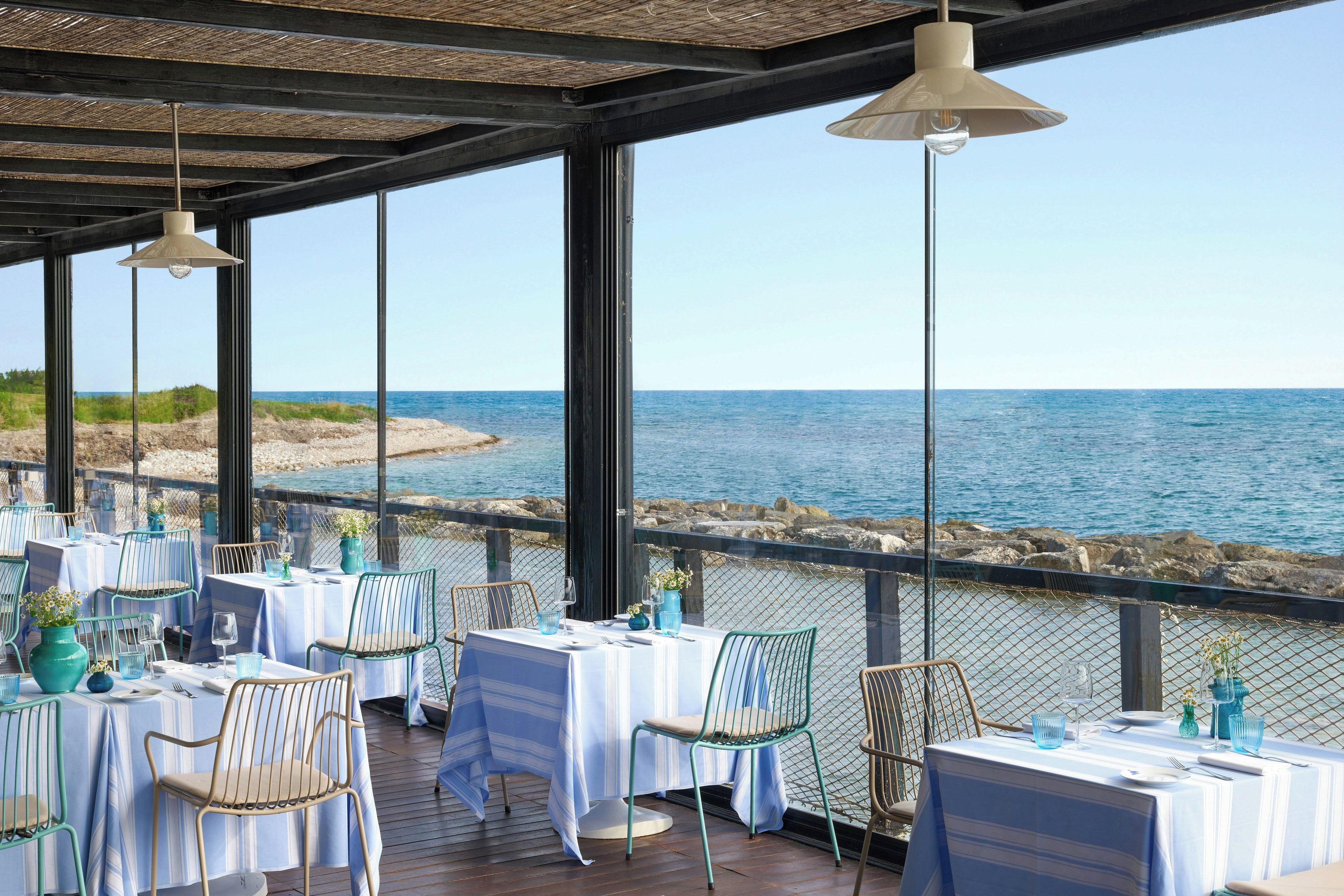 An outdoor dining area with tables and chairs, overlooking a body of water.