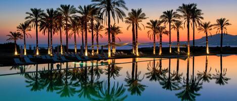 A poolside area with lounge chairs and palm trees against a sunset backdrop.
