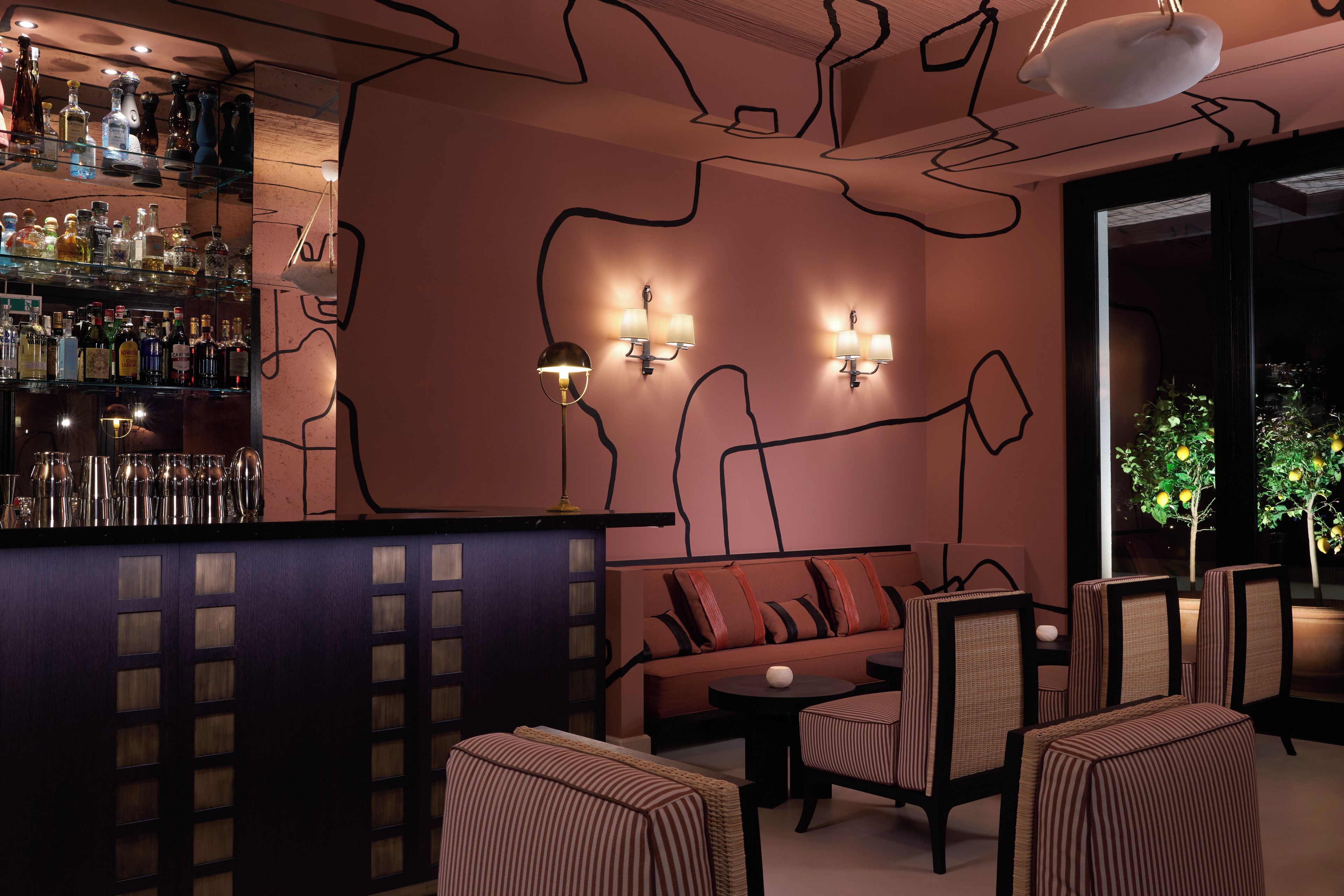 Un espace bar avec un assortiment de bouteilles d’alcool, un canapé avec des coussins et un coin salon composé de chaises.