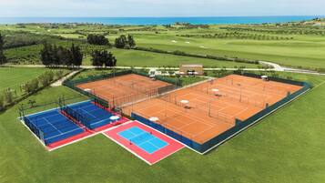 A tennis court complex with multiple courts, a golf course, and a view of the ocean.