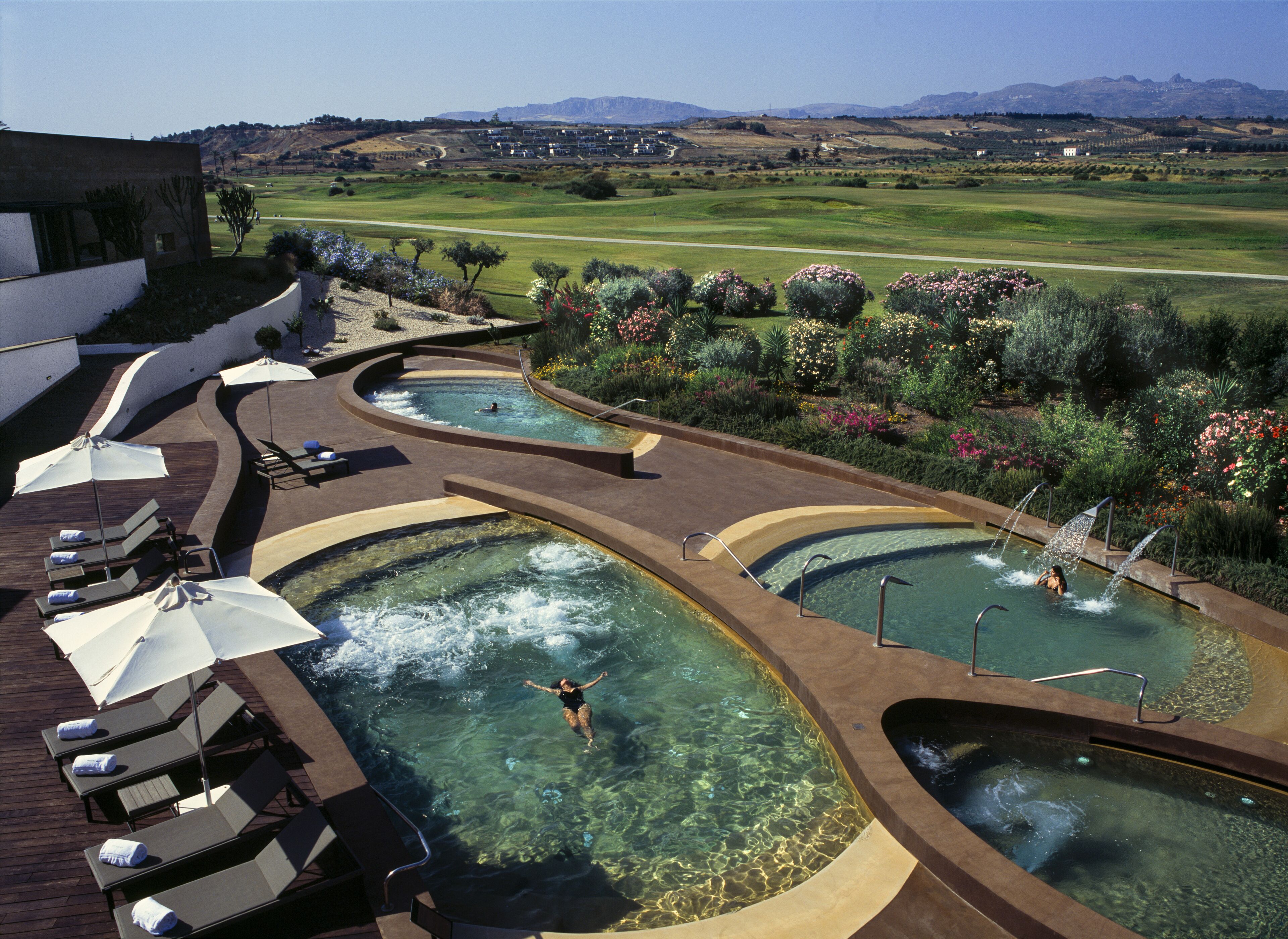 Un resort con varias piscinas, sillas de descanso y vistas a un campo de golf.
