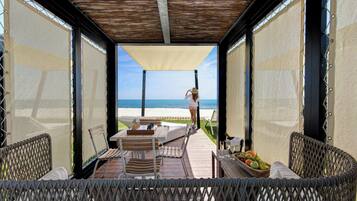 An outdoor seating area with a view of the beach, a table with chess pieces, and a fruit bowl.