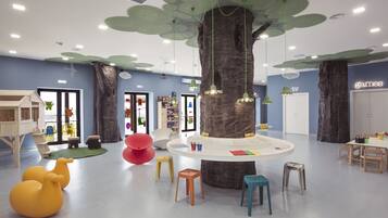 Children can play and learn in this vibrant play area with a tree-like structure, wooden house, and shelves of toys and books.