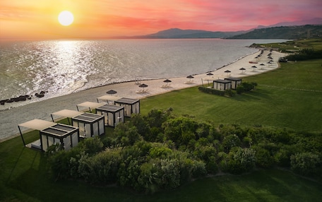A coastal resort with a beach, sun loungers, and a view of the sunset over the sea.