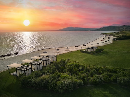 A coastal resort with a beach, sun loungers, and a view of the sunset over the sea.