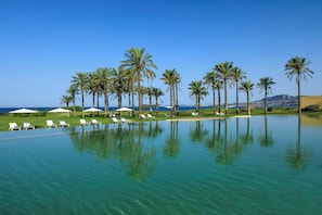 A poolside area with lounge chairs and umbrellas, surrounded by palm trees, under a clear sky.