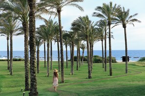 A woman walking on a golf course with palm trees and a view of the ocean. - Verdura Resort (Sciacca)