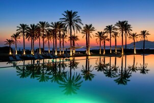 A poolside area with lounge chairs and palm trees at sunset.