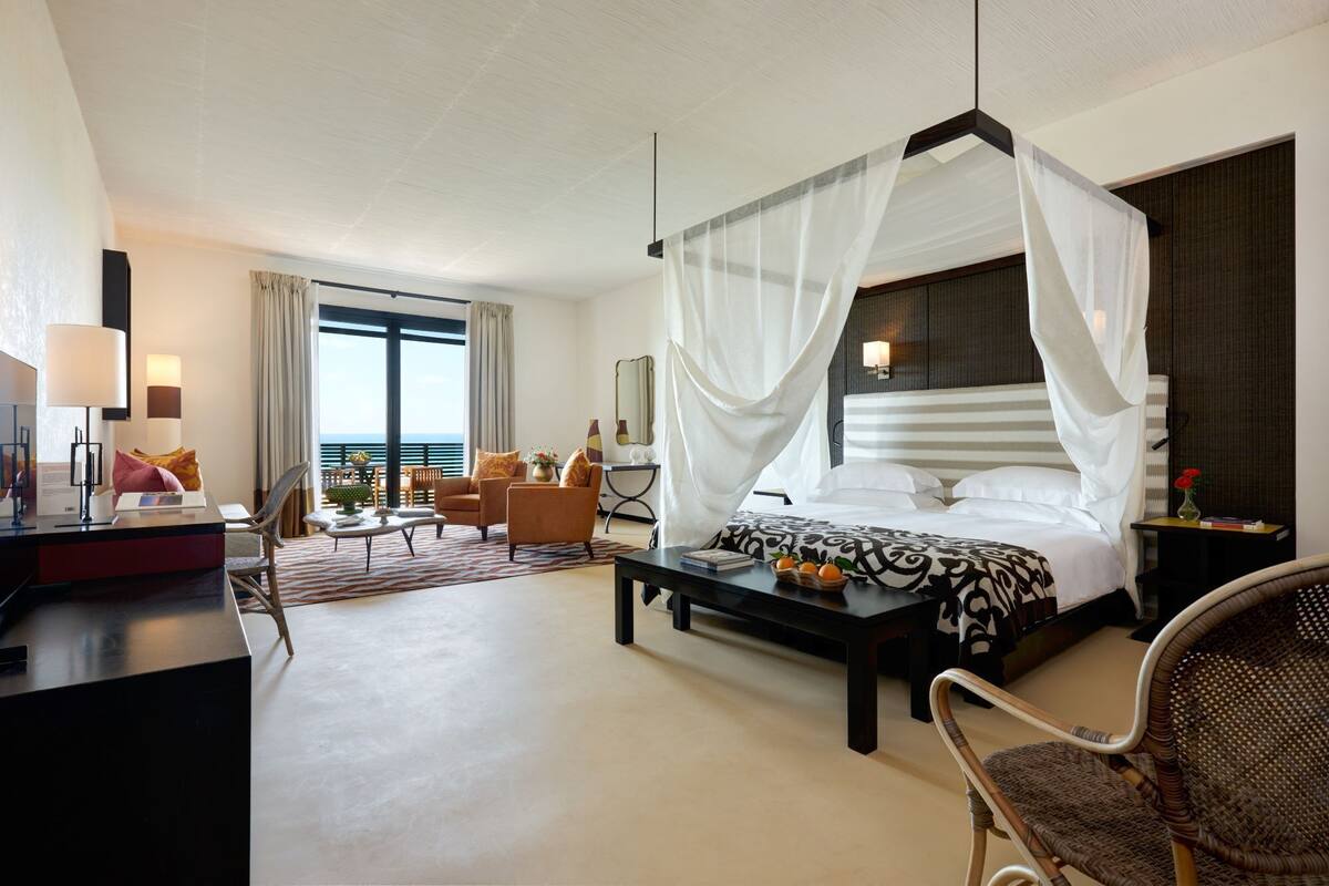 A hotel room with a large bed, a desk, a chair, and a view of the sea.
