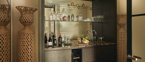 Una zona de bar con estantes llenos de botellas, vasos y un frutero.