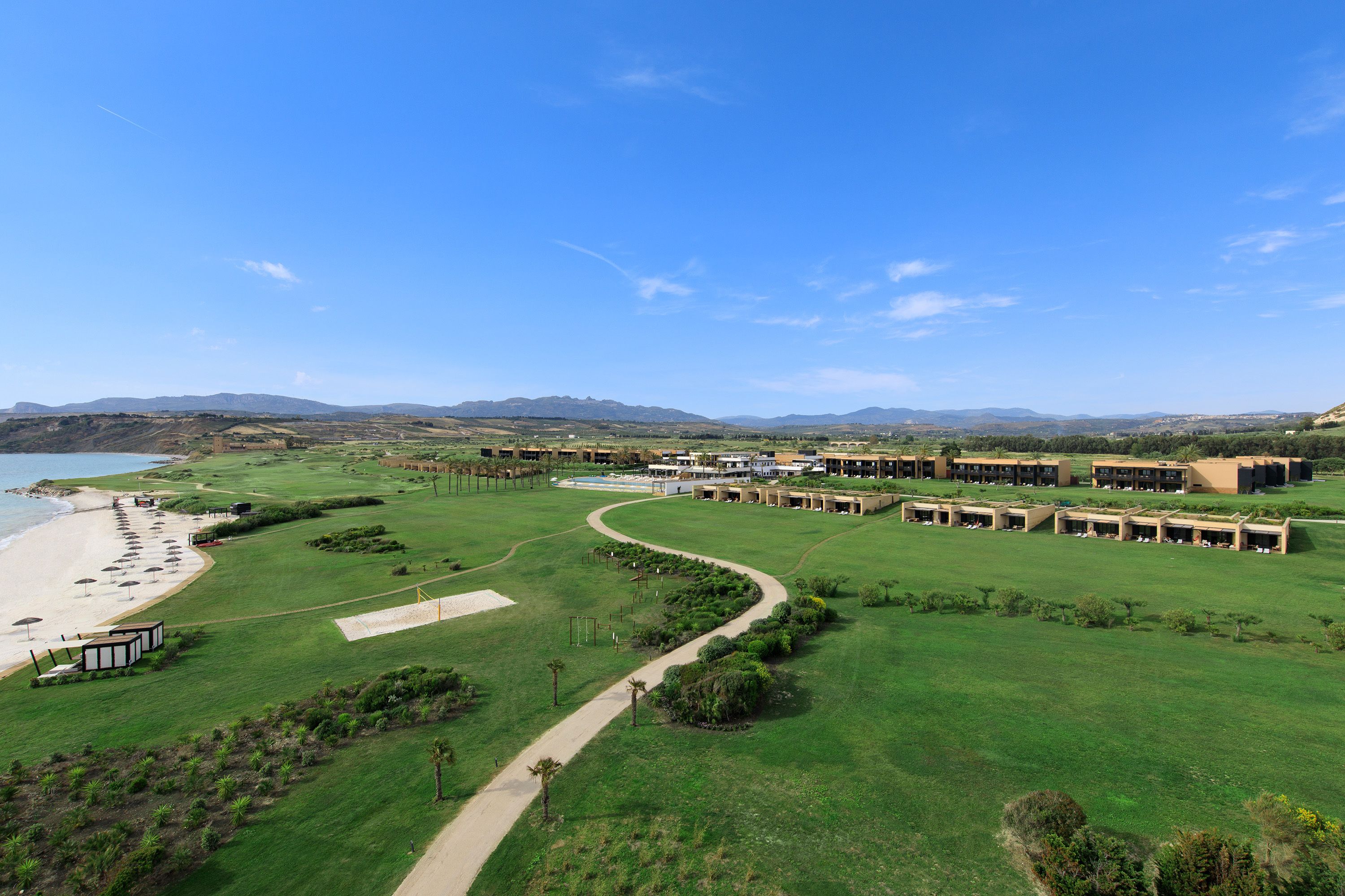 Um campo de golfe com uma praia, um caminho e uma fileira de edifícios.