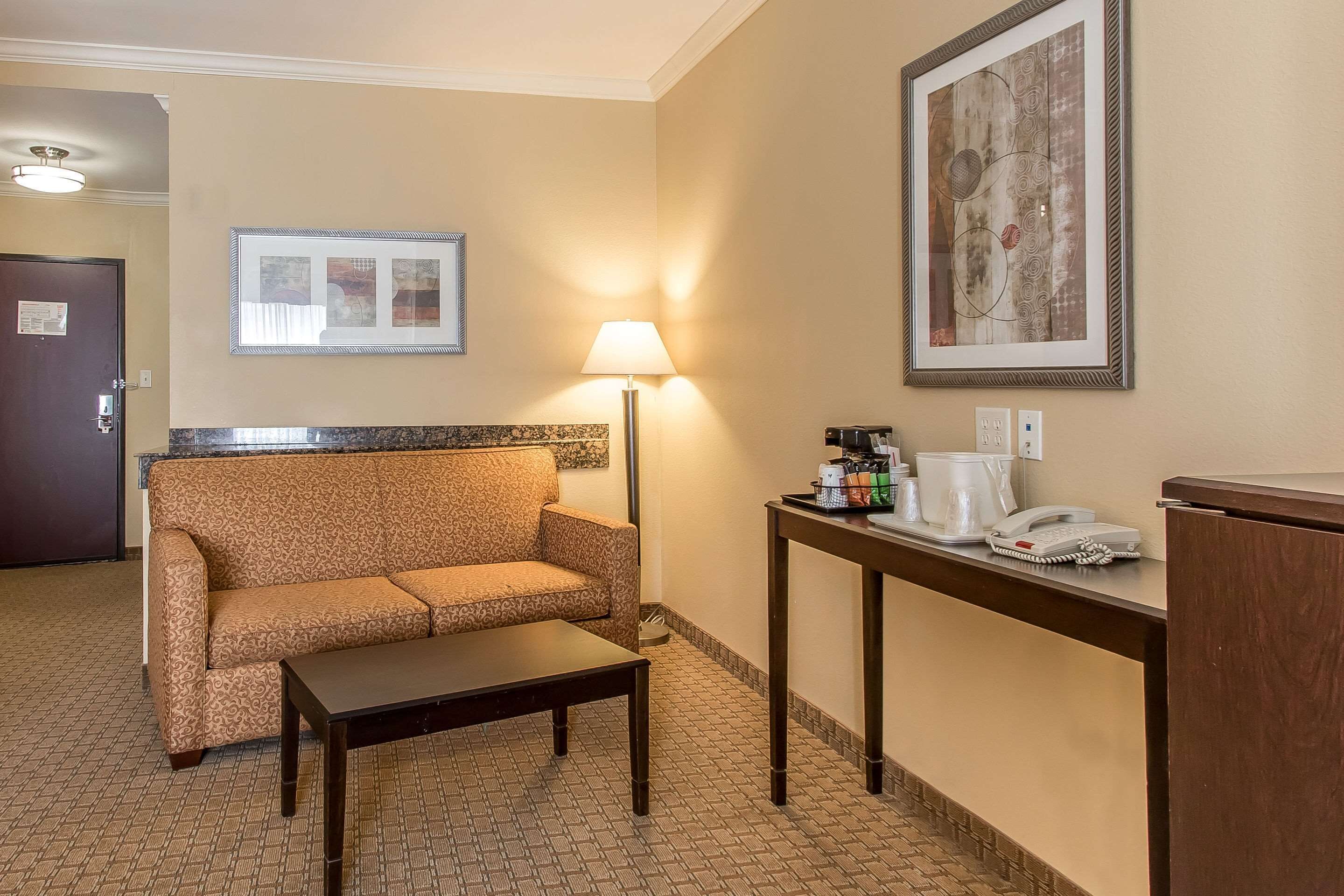 A hotel room with a sofa, a small table, a lamp, a coffee station, and a framed picture on the wall.