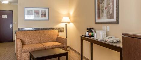 A hotel room with a sofa, a small table, a lamp, a coffee station, and a framed picture on the wall.