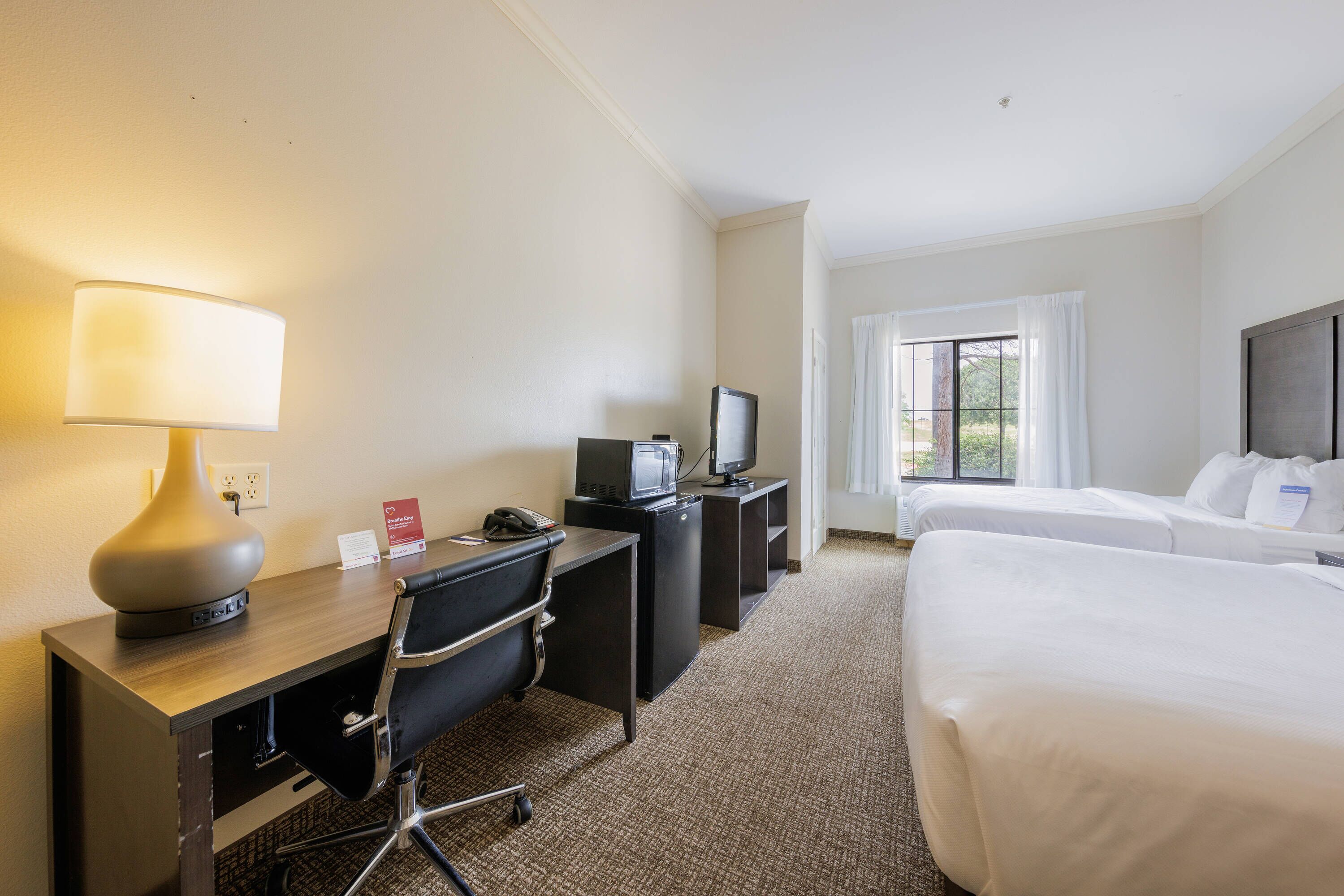 Ett hotellrum med ett skrivbord, en stol, en TV och två sängar.