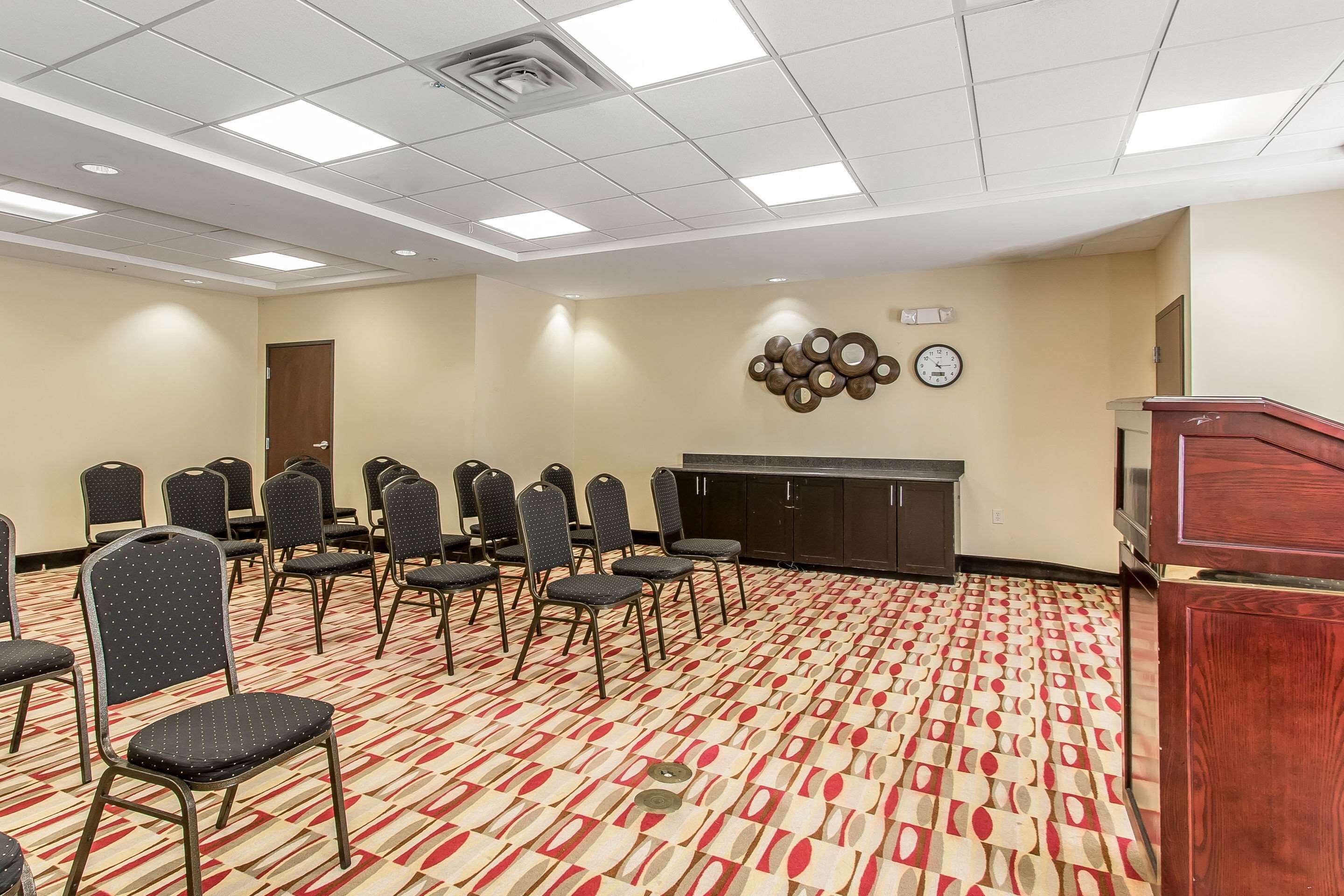 A conference room with rows of chairs, a podium, and a clock on the wall.