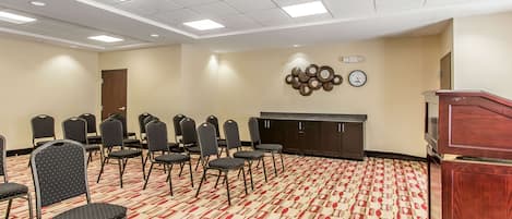 Un salón de conferencias con filas de sillas, un atril y un reloj en la pared.