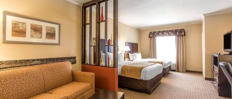 Quarto de hotel com sofá, cama, escrivaninha, televisão e uma grande janela com cortinas.