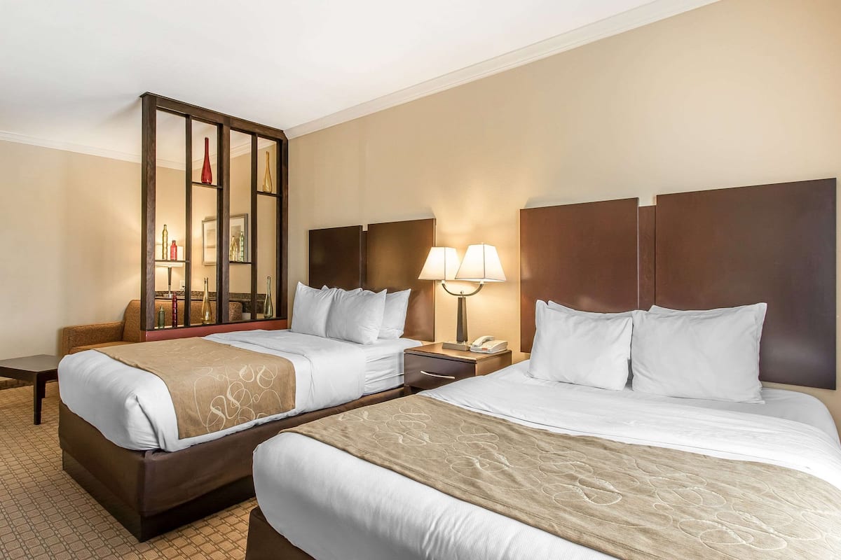Habitación de hotel con dos camas, un espejo grande, lámparas de noche y una mesita con lámpara.