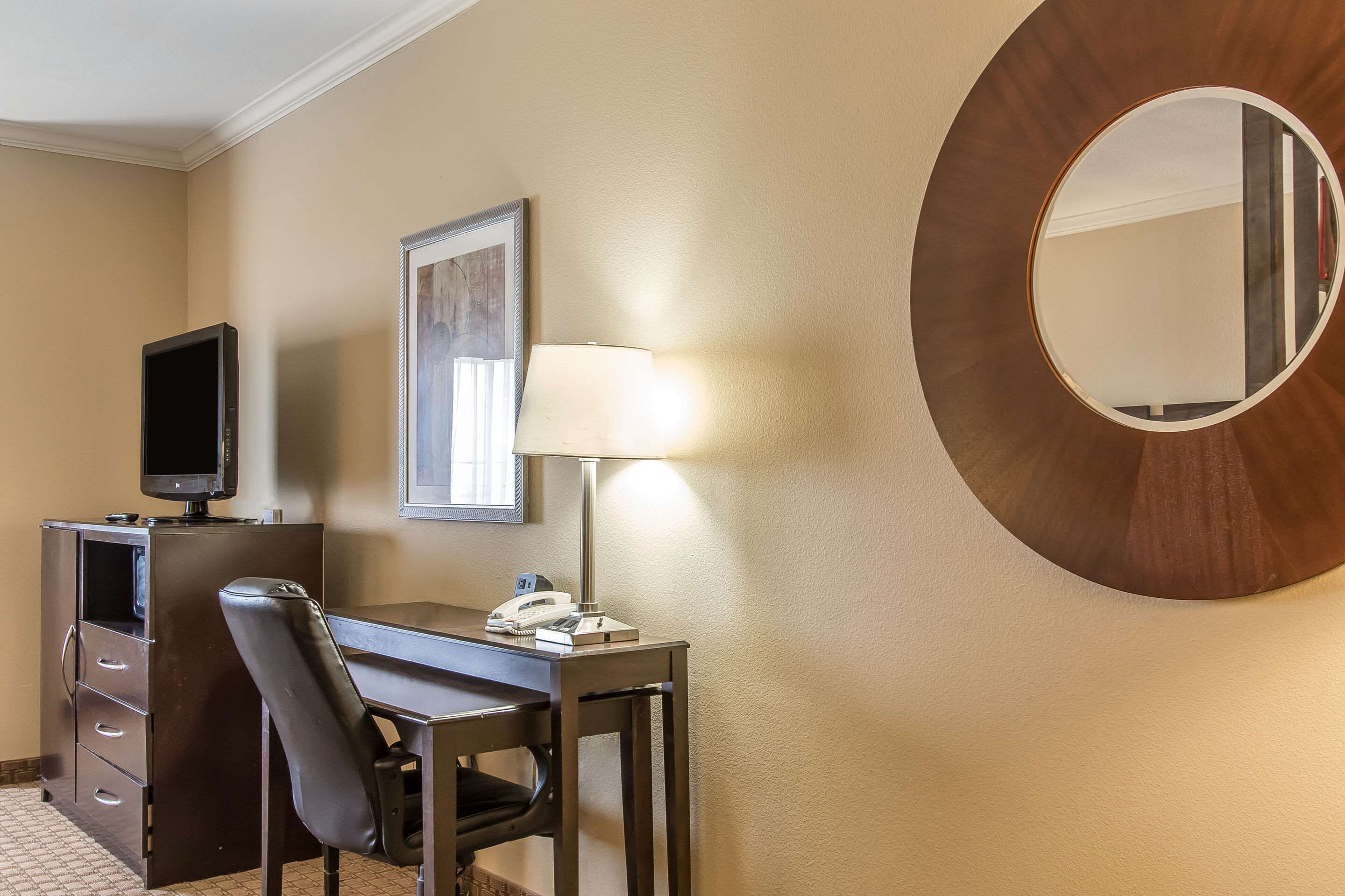 Ein Hotelzimmer mit Schreibtisch, Stuhl, Fernseher, Lampe und einem großen Spiegel.