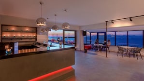 Een moderne keuken met een bar, grote ramen met uitzicht op zee, en een eethoek met een tafel en stoelen.