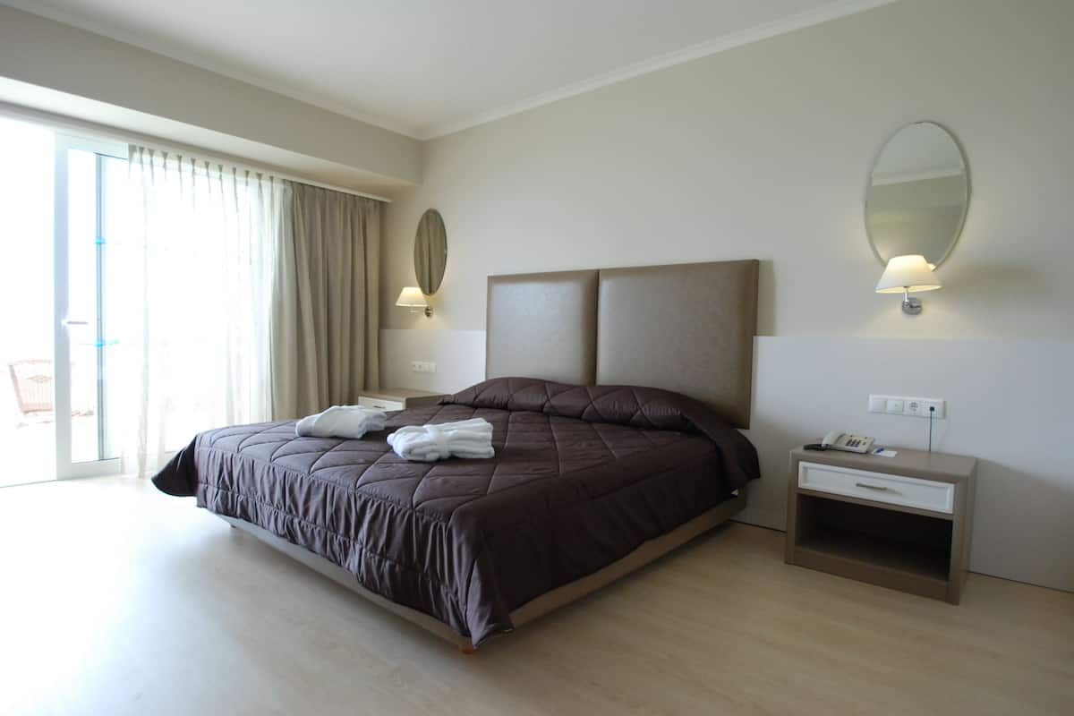 Un grand lit avec une tête de lit, une table de chevet avec une lampe, un miroir et une vue sur l’extérieur grâce à une grande fenêtre.