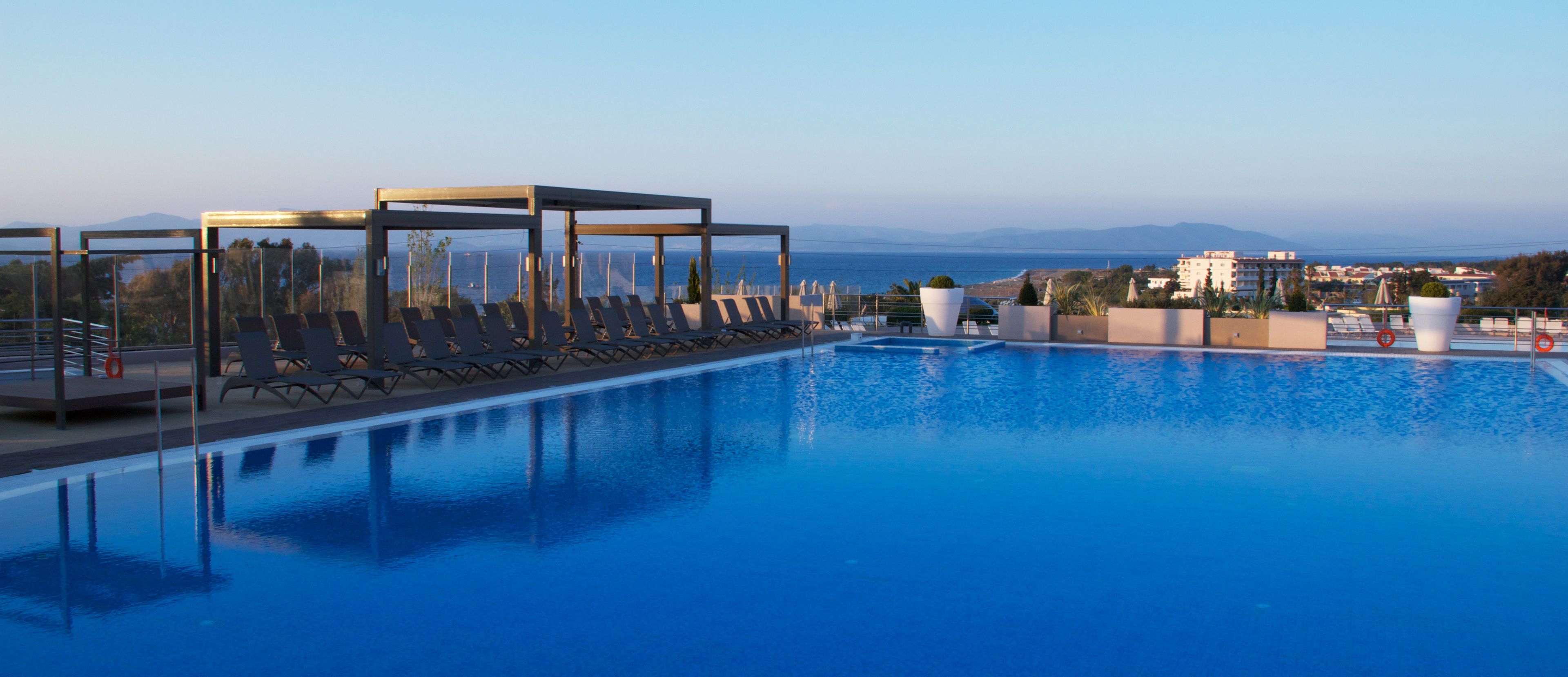 Ein Pool mit Liegestühlen und einer überdachten Lounge, mit Blick auf eine Küstenstadt.