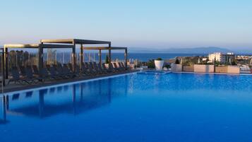 Ein Pool mit Liegestühlen und einer überdachten Lounge, mit Blick auf eine Küstenstadt.
