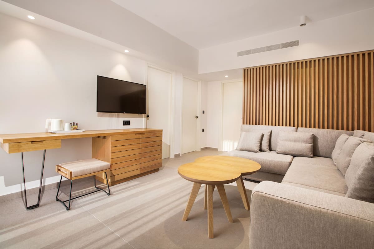 A modern living room with a sofa, a wooden coffee table, a TV on a wall, and a desk with drawers.