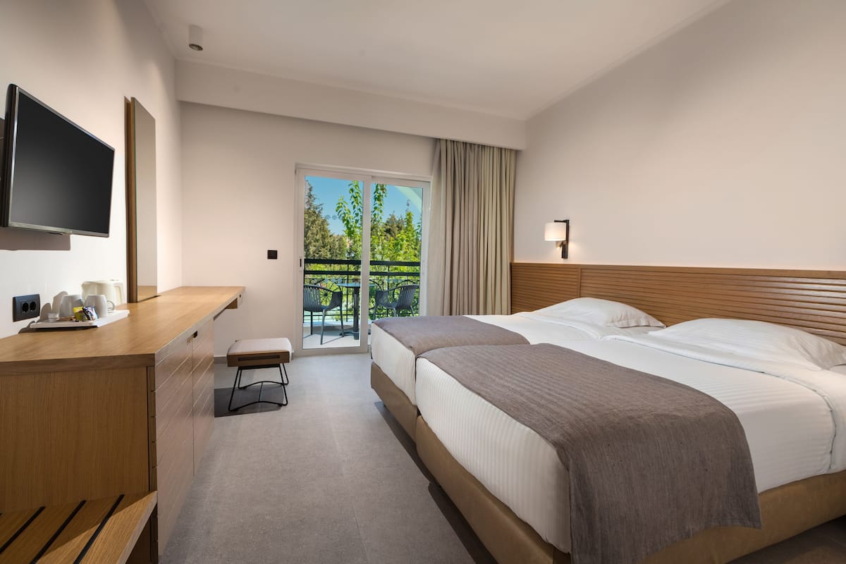 A hotel room with a bed, a desk, a television, and a balcony with outdoor seating.