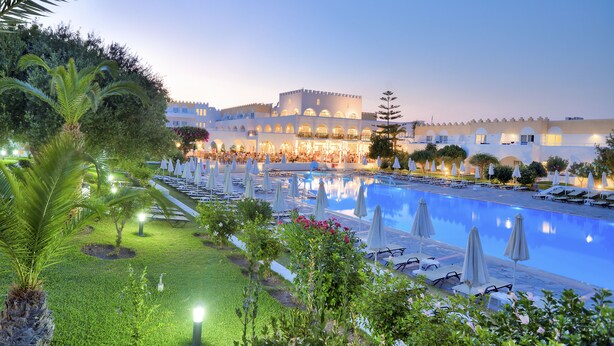 A hotel with a large pool, sun loungers, and a well-lit outdoor dining area. - Hotel Platanista (Kos)